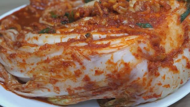Person picking up traditional kimchi with plastic gloved hands