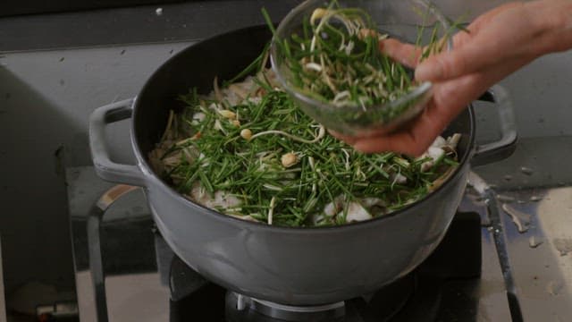 Adding fresh greens to a pot on a stove