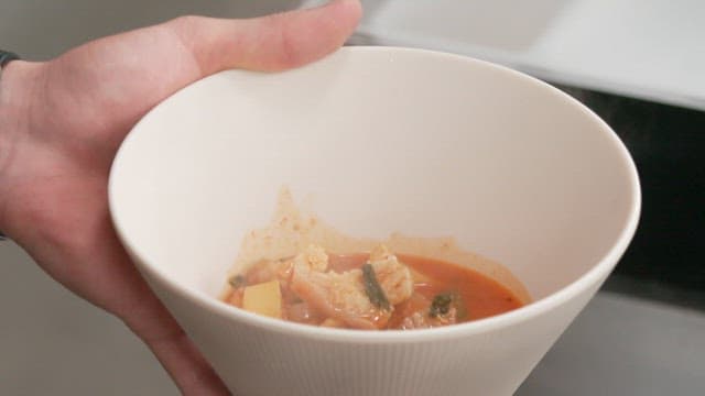 Pouring steaming pork stew into a bowl in the kitchen