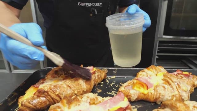 Croissants being brushed with egg wash in a bakery kitchen