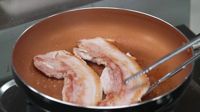 Pork belly slices being cooked in a pan