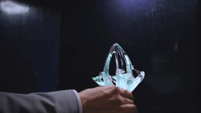 Man examining a glowing, intricate glass artifact in a dimly lit room