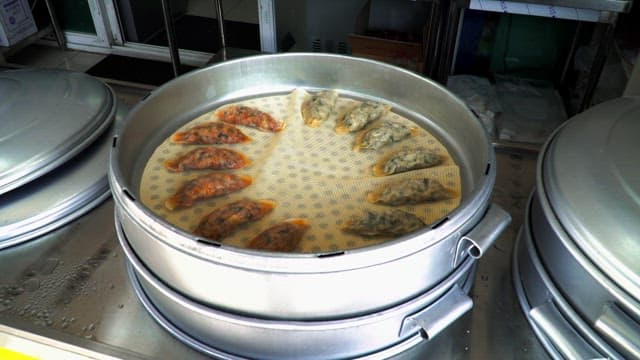 Meat dumplings, kimchi dumplings, and steamed bun being prepared at a large steamer