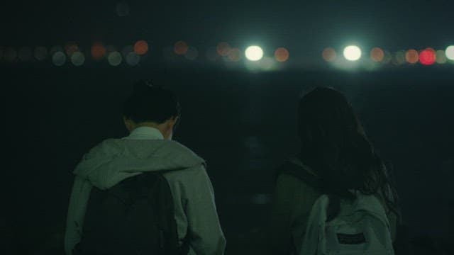 Two students sitting side by side on a beach with lights shining on them
