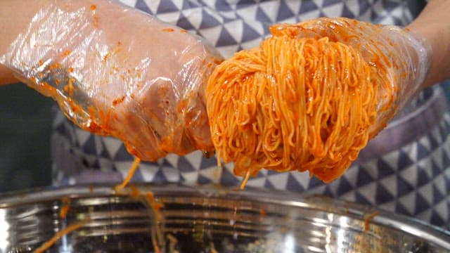 Plastic gloved hands plating spicy bibim noodles into a bowl