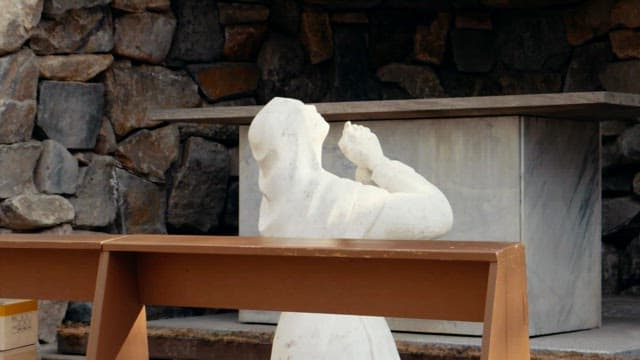 Statue of woman praying with a stone sculpture of Virgin Mary in a rocky outdoor shrine