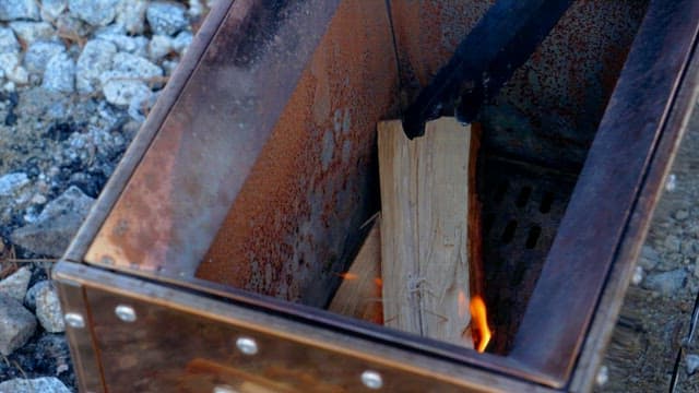Lighting a fire in an outdoor fire pit with wood and tongs