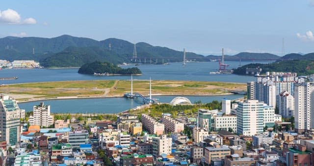 Cityscape with buildings, mountains and sea under the sky from day to night