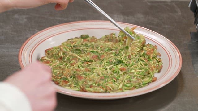 Picking up zucchini pancakes on a plate with chopsticks