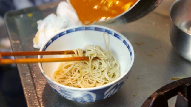 Pouring curry sauce over noodles in a bowl
