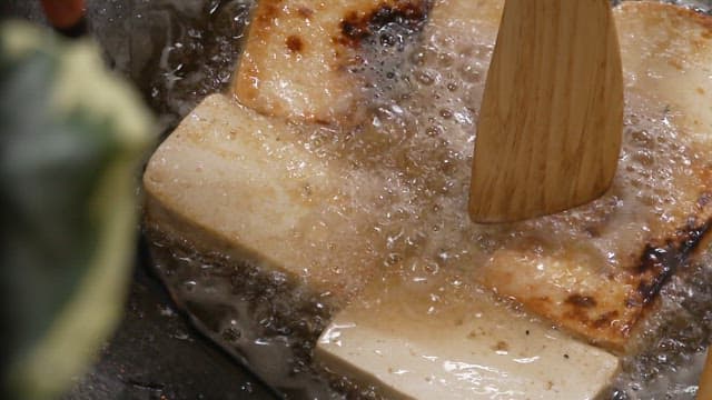 Frying tofu on a frying pan with wooden spatula