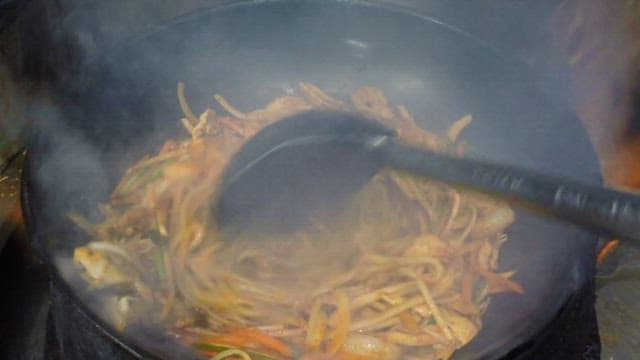 Cooking spicy stir-fried jjamppong with vegetables in a wok