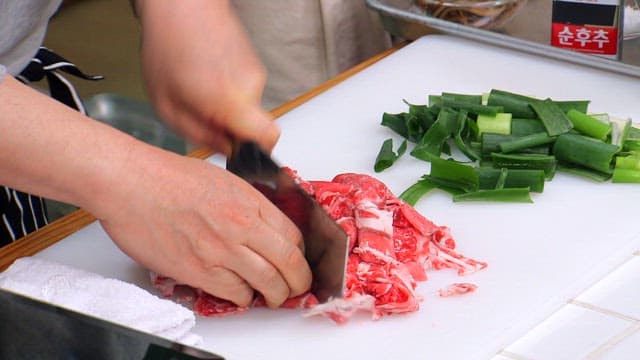 Slicing beef and green onions on a cutting board