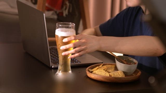 Person enjoying a beer and snacks while using a laptop