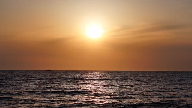 Sunset over the ocean with a distant boat