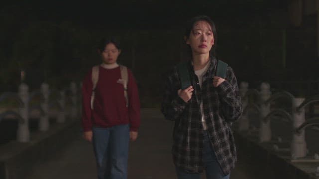 Woman with a scar on her face walking down the street at night with a woman walking behind her