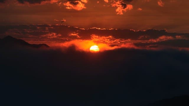 Sun setting behind mountains and clouds