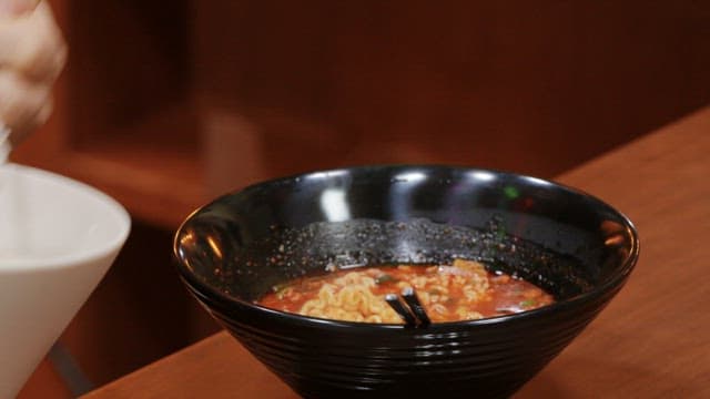 Black bowl of spicy ramen with rice in it