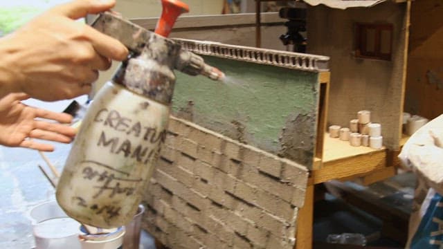 Model maker carefully painting a miniature building.