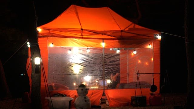 Cozy orange tent at night with a snowman perched in front