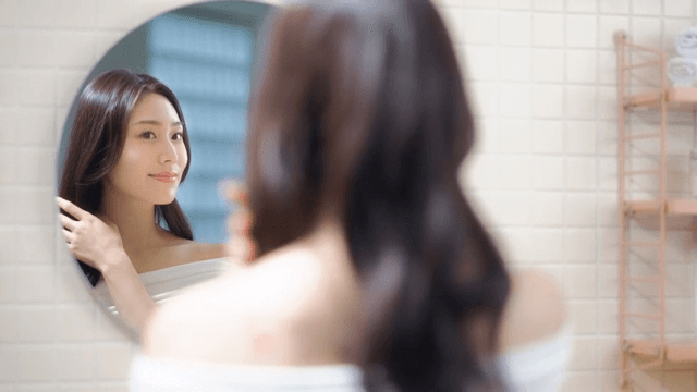 Woman smiling while touching her hair in front of bathroom mirror