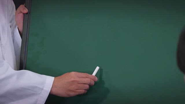 Person writing on a chalkboard with a chalk in the classroom