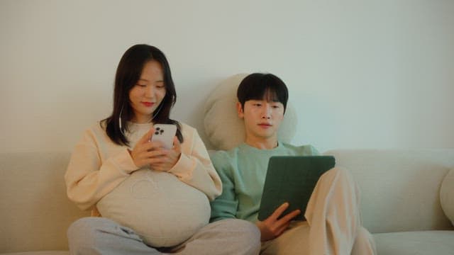 Two people using digital devices on a sofa in cozy living room