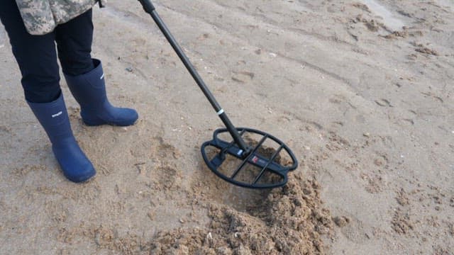 Person using a metal detector and shovel on a sandy beach