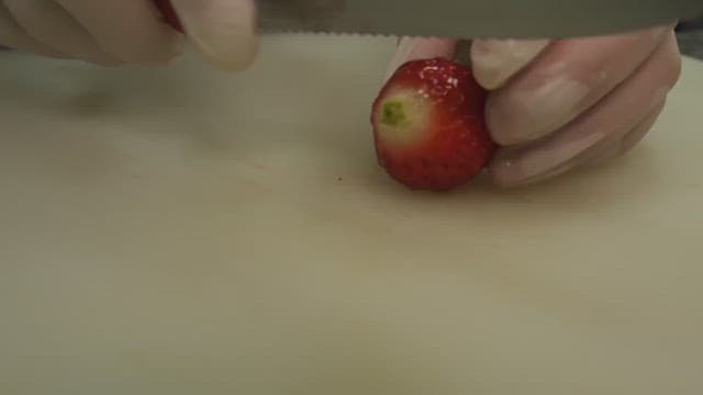 Hands slicing a strawberry on a cutting board