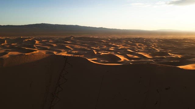 People climbing a large sand dune at sunset