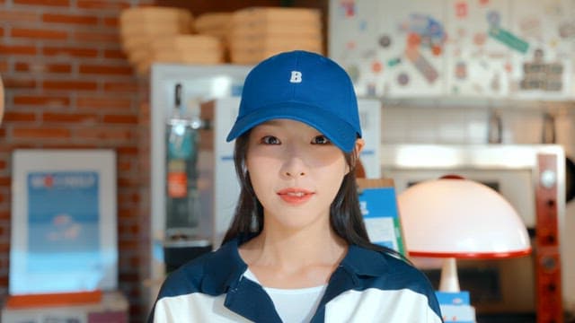 Smiling woman in a pizza shop wearing a blue cap