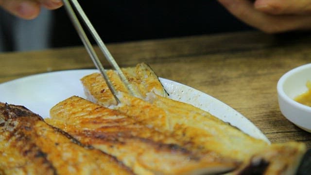 Grilled spanish mackerel being flaked with chopsticks