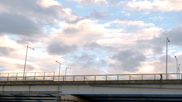 Sunset clouds over a bridge with cars and people walking by