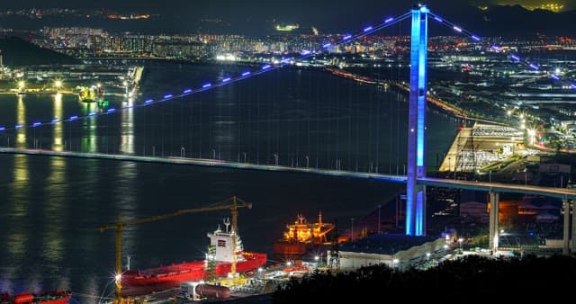 Illuminated Ulsan Bridge over a bustling harbor at night