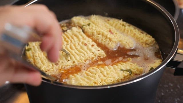 Stirring ramen noodles boiling in a pot with tongs