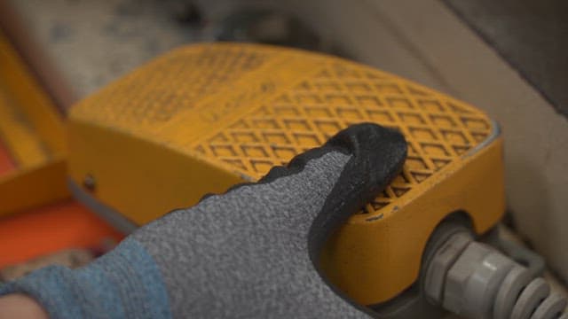 Gloved hand pressing a yellow pedal