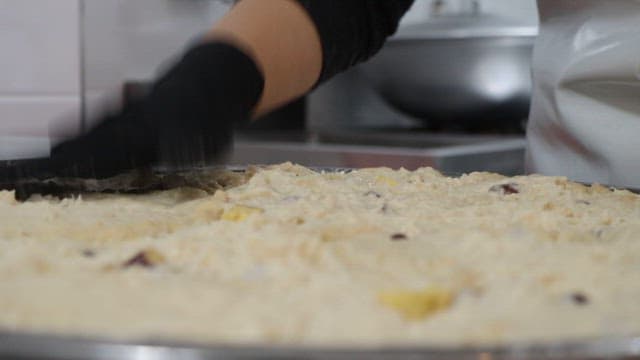 Mixing dough with gloved hands in a kitchen.