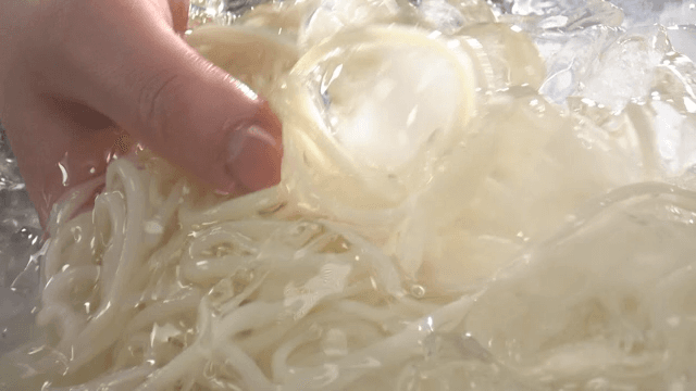 Hands rinsing noodles in a bowl of cold water
