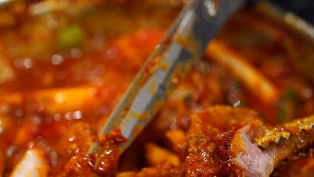 Cutting the meat of the spicy braised ribs boiling on the gas stove