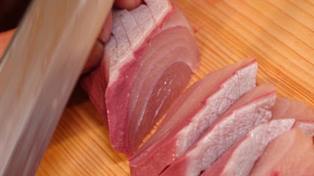Slicing fresh yellow tail on a wooden board