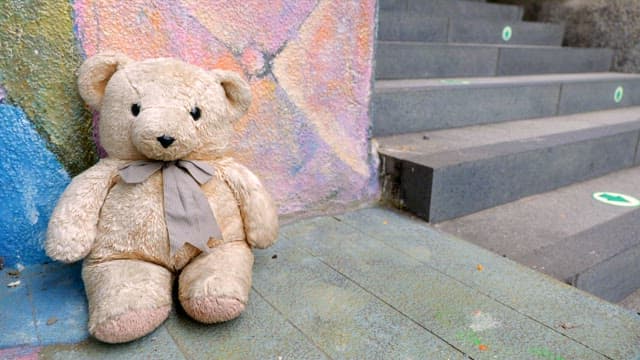 Teddy bear leaning against a colorful wall next to the stairs