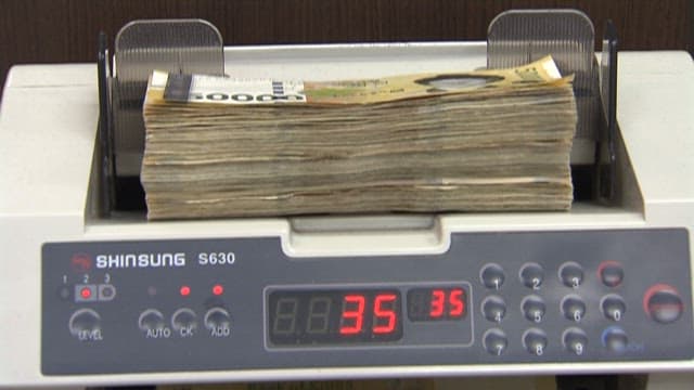 Employee counting 10,000 won notes on a counter at a bank