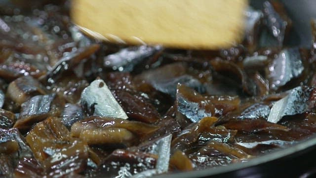 Stir-frying the half-dried saury with a wooden spatula in an oiled frying pan
