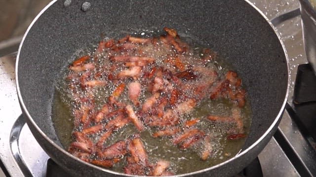 Sizzling bacon frying in oil on a stovetop in a kitchen.
