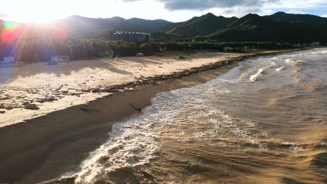 Vast beach with distant mountains and gentle waves under the sunny sky