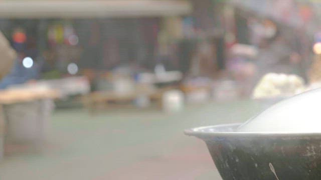 People walking by a steaming pot in a marketplace