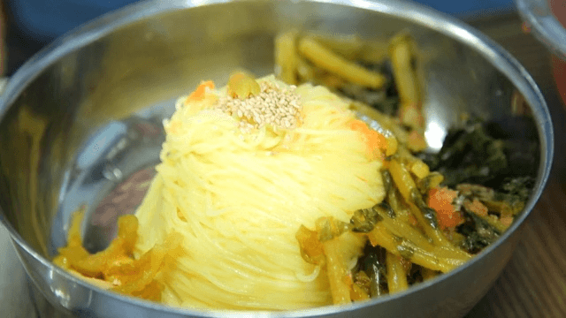 Adding yeolmu kimchi to cold noodles in a bowl