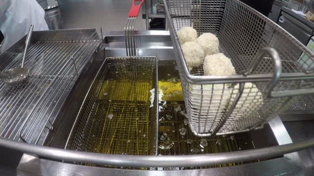 Putting potato croquette batter into a deep fryer full of oil in a commercial kitchen