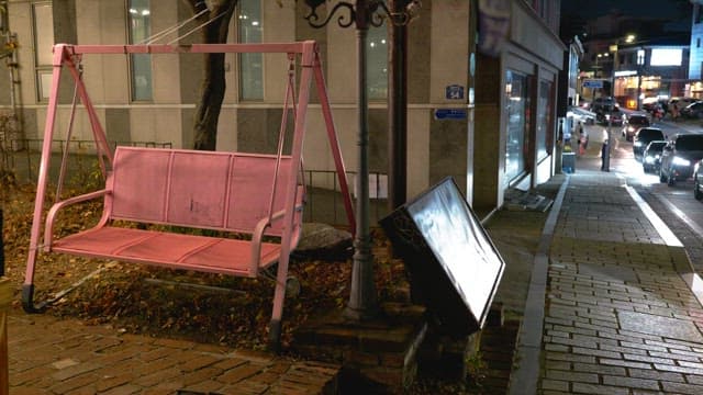 Pedestrians and cars passing by on a street lined with decorative pink swings