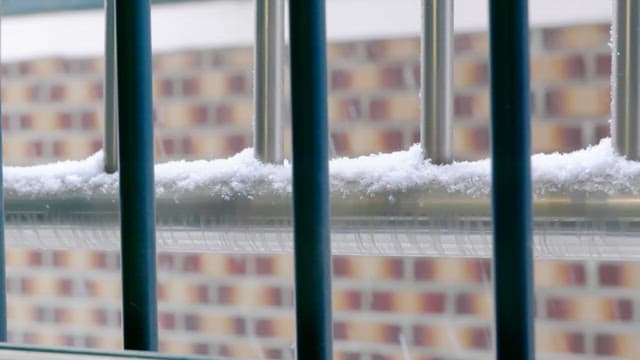 Snow-covered railing against a brick wall